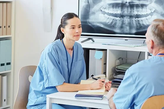 Une professionnelle en tenue bleue échange avec un homme devant une radiographie dentaire.