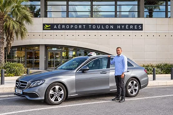 Un homme se tient près d’un taxi Mercedes gris devant l’entrée de l’aéroport Toulon Hyères.