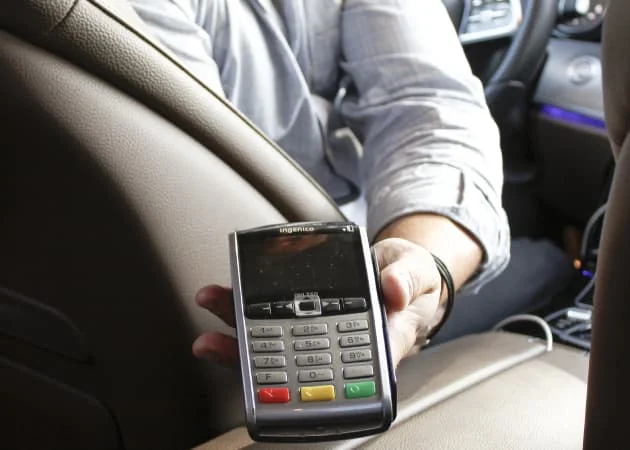 Une personne présente un terminal de paiement à l’arrière d’une voiture.